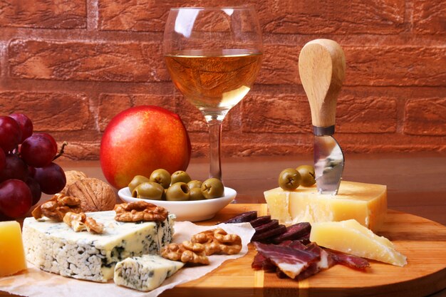 Variedade de queijo com frutas, uvas, nozes e faca de queijo em uma bandeja de servir de madeira.