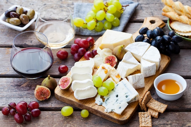Variedade de queijo e frutas na tábua com vinho branco tinto em fundo de madeira
