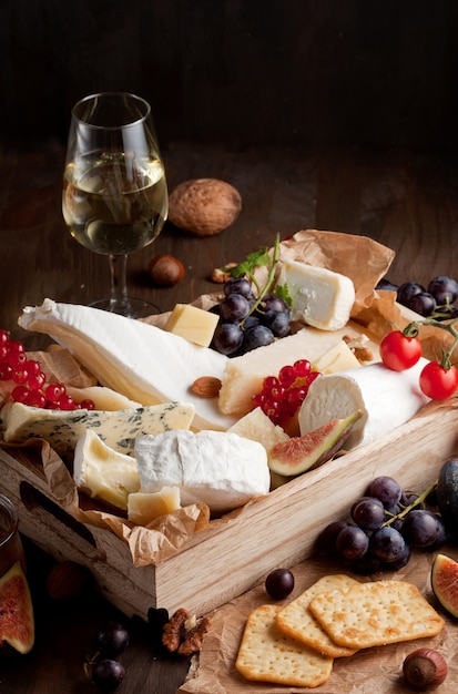 Variedade de queijos diferentes com vinho, frutas e nozes. Camembert, queijo de cabra, roquefort, gorgonzolla, gauda, parmesão, emmental, brie