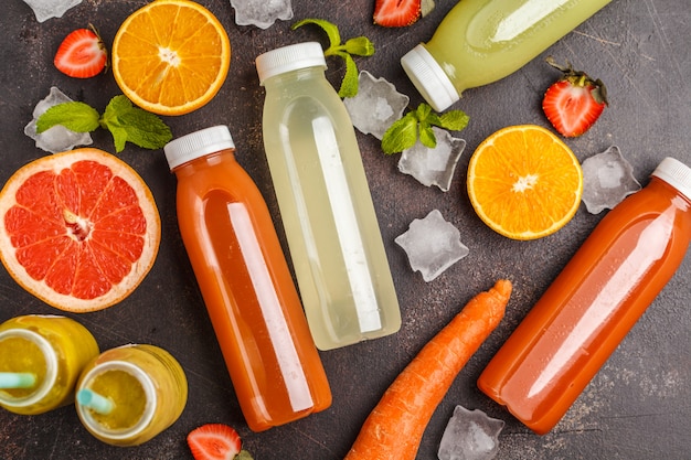 Variedade de smoothies coloridos ou garrafas de sucos de frutas, frutas e vegetais, vista de cima, mesa escura. Programa de desintoxicação, conceito de estilo de vida saudável.