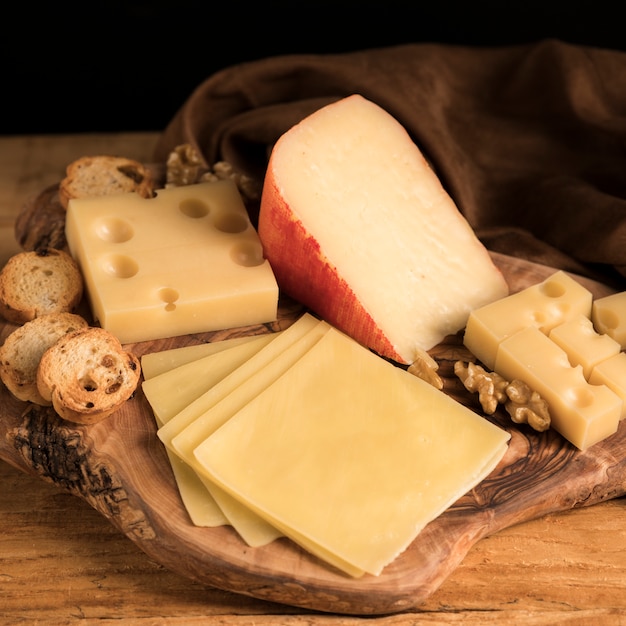 Variedade fresca de queijos com noz e pão na bandeja textured de madeira