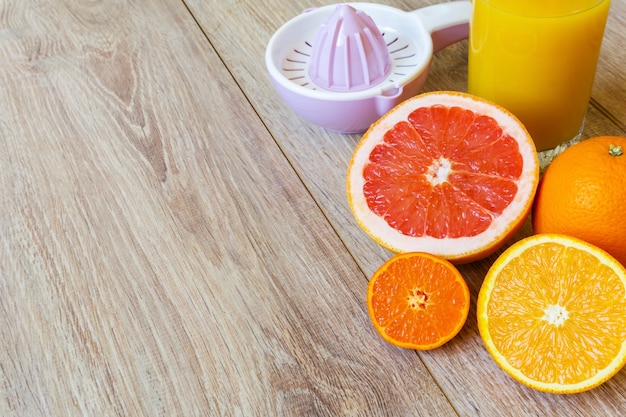 Vários alargadores manuais inteiros e cortados de frutas cítricas e um copo de suco de laranja em uma mesa de madeira