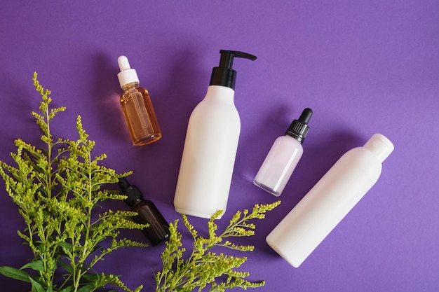 Vários blottles simulados diferentes com cosméticos e flores em fundo roxo