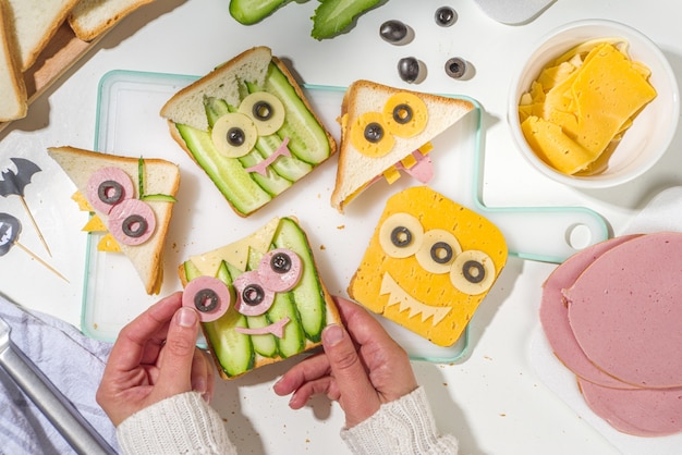 Foto varios bocadillos divertidos de halloween de monstruos. cocinar tostadas de bocadillos de desayuno creativos con queso, comida de fiesta de niños de halloween, manos de mujer madre en la vista superior de la imagen