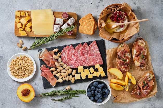 Varios bocadillos de vino gourmet. Arándanos, melocotones, galletas saladas, salami, prosciutto, bruschetta, pistacho, piñones, quesos variados, camembert y hierbas. Aperitivos italianos para unas vacaciones importantes.