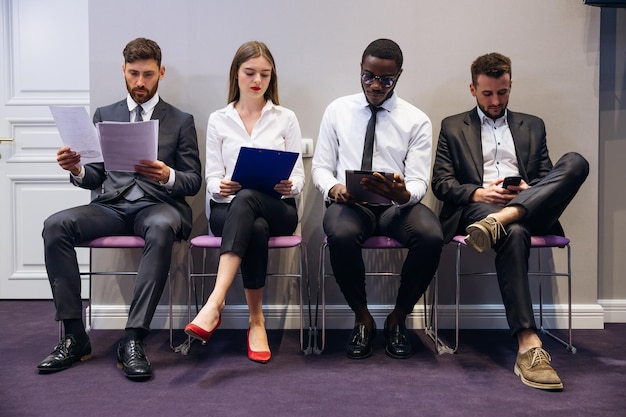 Vários candidatos a emprego sentam-se na fila esperando uma entrevista olhando através de gadgets contratando o conceito de gestão de pessoal