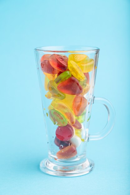 Varios caramelos de gelatina de frutas en vaso sobre fondo azul pastel