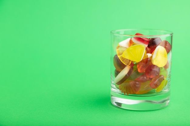 Varios caramelos de gelatina de frutas en vaso sobre fondo verde copia vista lateral del espacio