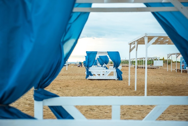 varios cenadores en la playa al atardecer con cortinas azules plegables sin gente