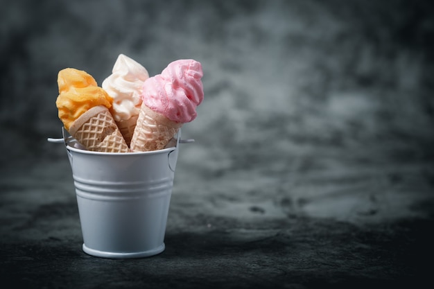 Varios de colorido cono de helado de merengue en el cubo sobre un fondo oscuro para el concepto de postre dulce y refrescante