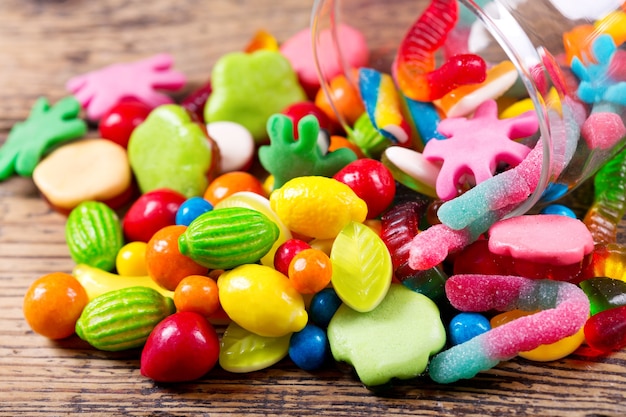 Varios coloridos caramelos, jaleas y mermeladas en frasco de vidrio sobre mesa de madera