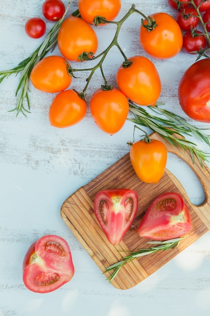 Varios coloridos tomates y hierba de romero sobre una superficie azul claro