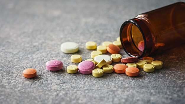 Foto vários comprimidos e pílulas médicas multicoloridas derramando de um frasco de drogas pílulas e drogas indústria farmacêutica fundo de mármore cinza escuro