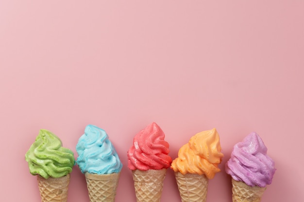 Varios conos de helado de merengue de colores sobre fondo rosa para un concepto de postre dulce y refrescante
