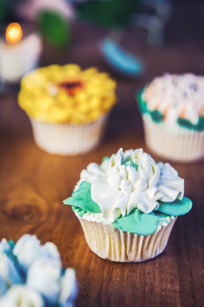 Varios cupcakes decorados con glaseado de flores de colores en la mesa de madera ramo floral pastel de bodas hola