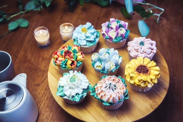 Varios cupcakes decorados con glaseado de flores de colores en la mesa de madera ramo floral pastel de bodas hola