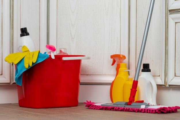 Vários detergentes de limpeza doméstica e garrafas em um balde de plástico no chão