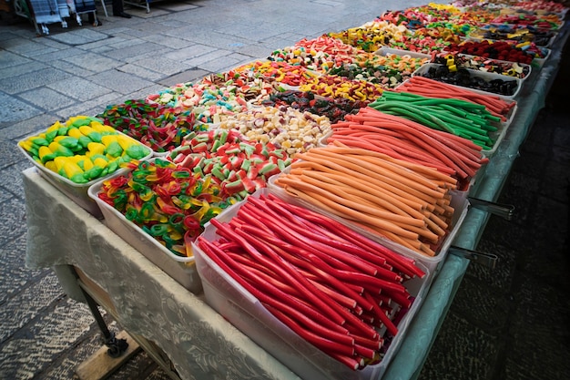 Vários doces gelatinosos coloridos e confeitos expostos em caixas plásticas à venda na rua. doces e lápis de cor contrastantes colocados à venda para os compradores de rua. atração infantil.