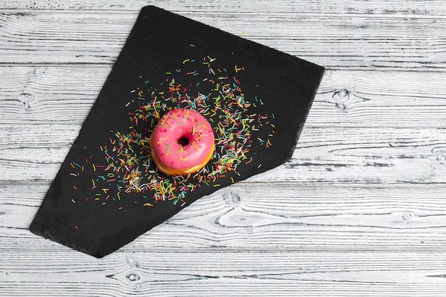 Vários donuts frescos em um prato de cerâmico preto em uma mesa de madeira