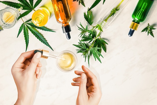 Vários frascos de vidro com óleo cbd, tintura de thc e folhas de cânhamo. óleo cosmético de cbd. mãos femininas segurando uma pipeta com óleo cosmético cbd