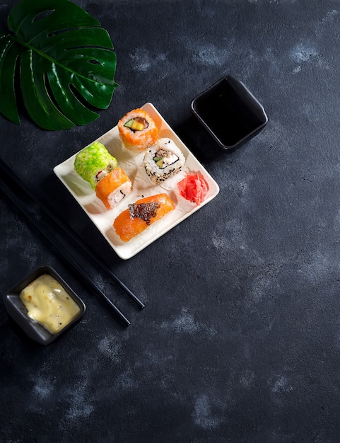 Varios frescos y deliciosos juegos de sushi en pizarra negra con palitos de pizarra, salsa sobre fondo de piedra negro