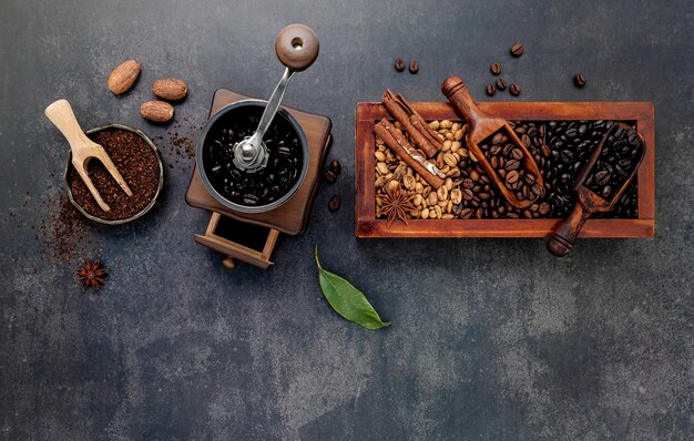Varios granos de café tostados en caja de madera con configuración manual de molinillo de café en piedra oscura.