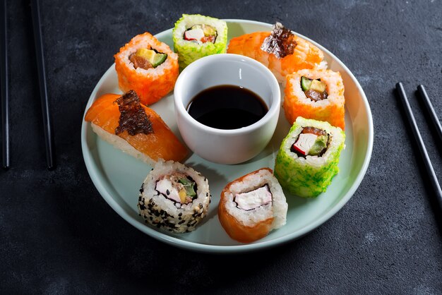 Varios juegos de sushi en placa de cerámica con palitos de pizarra, salsa en negro