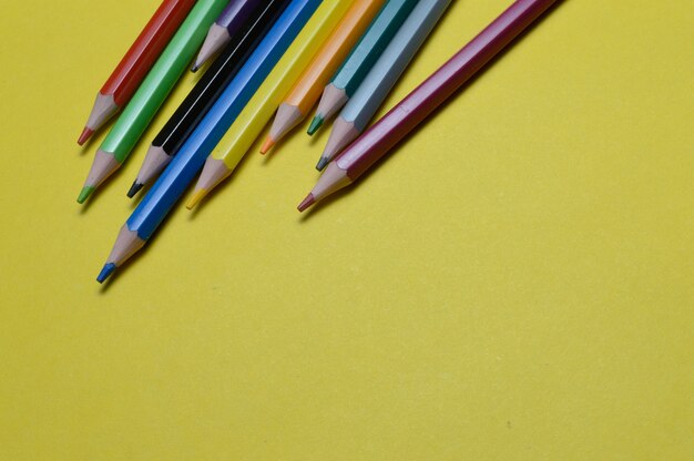 Vários lápis multicoloridos repousam na superfície amarela.