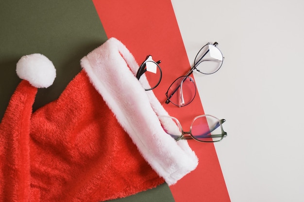 Vários óculos e chapéu de Papai Noel em fundo vermelho e verde, venda da loja de ótica antes do espaço da cópia do Natal