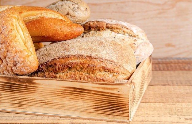 Vários pãezinhos crocantes rústicos e pão em uma caixa com um fundo de madeira.