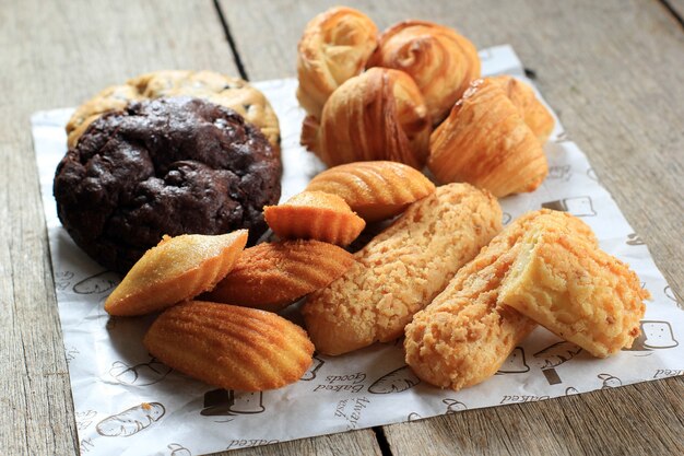 Varios pasteles de pastelería francesa sobre mesa de madera rústica. Madeleine, Craquelin Eclair, Mini Croissant, Galletas Grandes De Chocolate