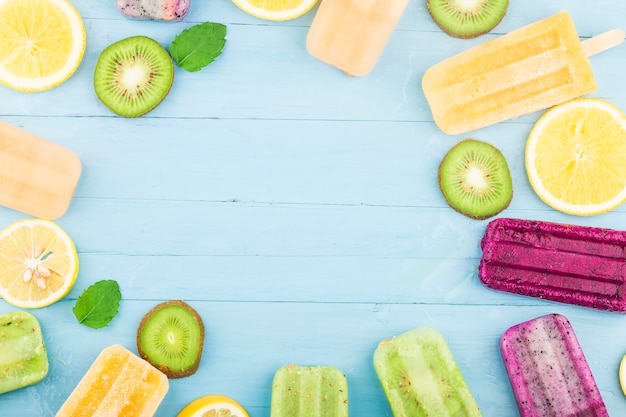 Foto vários picolés de frutas são colocados no fundo da placa de madeira azul, picolés de kiwi, picolés de laranja, picolés de fruta do dragão, picolé de melão