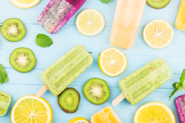 Vários picolés de frutas são colocados no fundo da placa de madeira azul, picolés de kiwi, picolés de laranja, picolés de fruta do dragão, picolé de melão