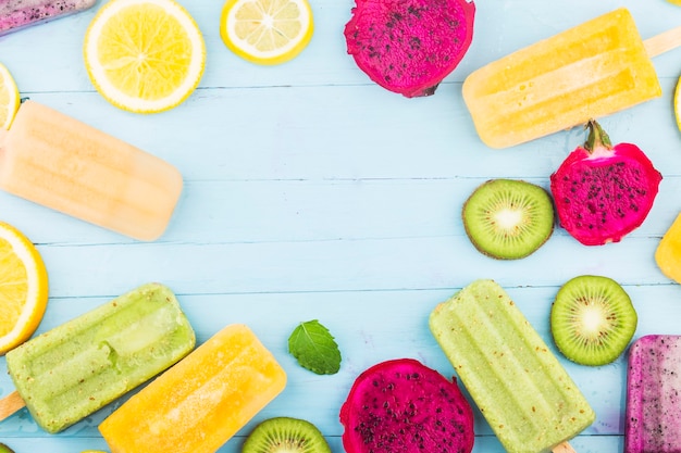 Vários picolés de frutas são colocados no fundo da placa de madeira azul, picolés de kiwi, picolés de laranja, picolés de fruta do dragão, picolé de melão