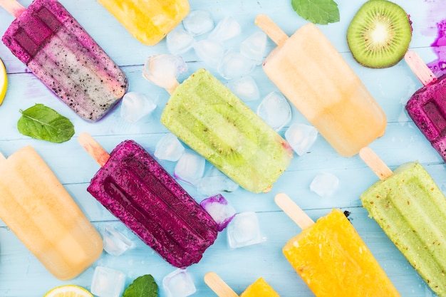 Vários picolés de frutas são colocados no fundo da placa de madeira azul, picolés de kiwi, picolés de laranja, picolés de fruta do dragão, picolé de melão