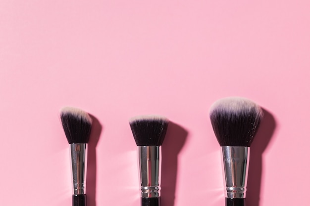 Varios pinceles de maquillaje sobre fondo rosa con espacio de copia, vista superior, cosméticos y concepto de belleza