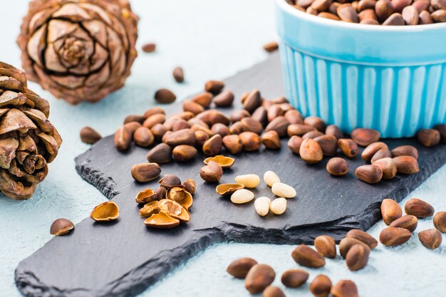 Varios piñones pelados entre nueces con cáscara sobre un tablero de pizarra. Remedio para el insomnio y la alimentación detox. Vitaminas y salud