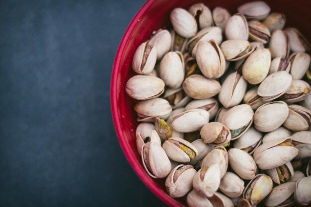 Varios pistachos dentro de un recipiente rojo con fondo negro