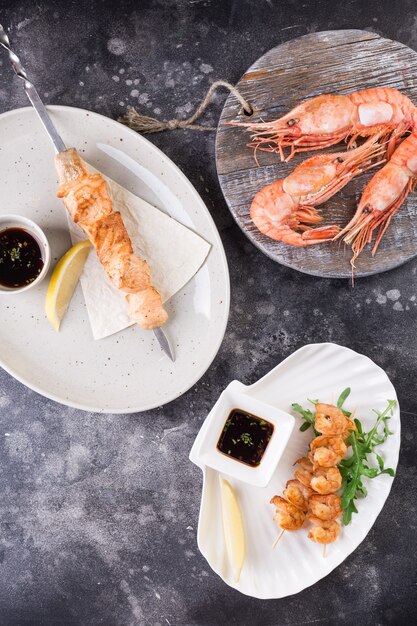 Varios platos. brochetas de salmón y camarones pelados con limón, salsa teriyaki y vegetación en platos blancos y grandes camarones en una tabla de madera.