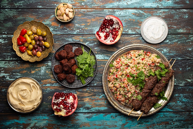 Foto varios platos turcos: kebab de carne con ensalada tabbouleh, falafel, hummus, aceitunas, pistachos y otros meze del medio oriente en la vista superior de la mesa de madera. comida étnica árabe, cocina de turquía