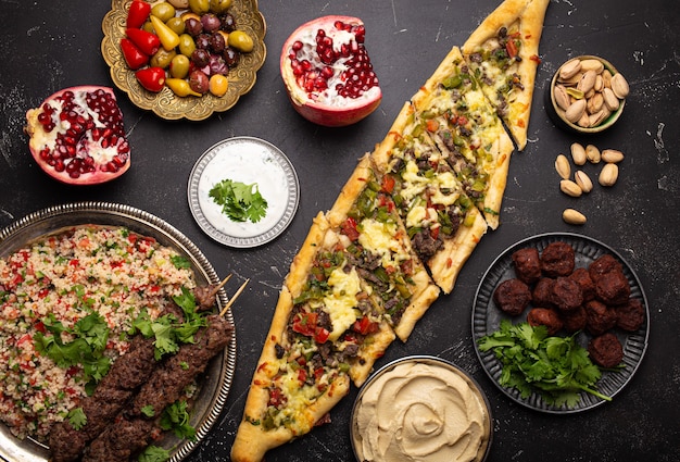 Varios platos turcos: pizza pide, kebab de carne con ensalada tabbouleh, falafel, hummus, aceitunas, pistachos y meze del Medio Oriente en la vista superior de la mesa de hormigón negro. Comida étnica árabe, cocina de Turquía