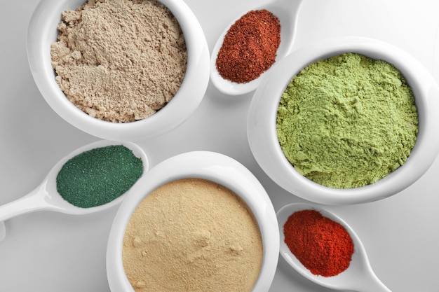 Vários pó de superalimentos coloridos em utensílios de cozinha em fundo claro