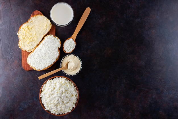 Vários produtos lácteos. Leite, queijo cottage e creme de leite em uma mesa escura