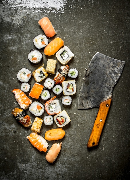 Vários rolos de sushi japonês com um machado para cortar. Na mesa de pedra.