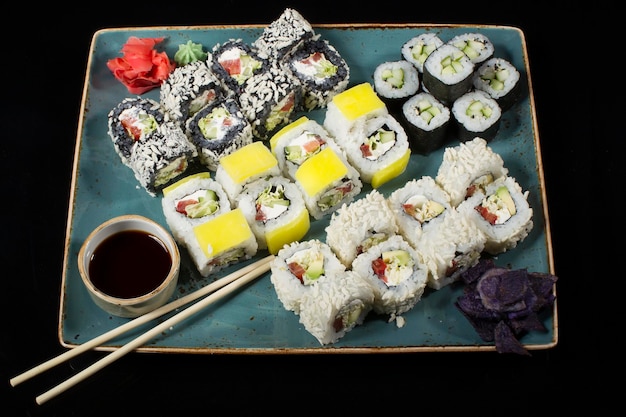Varios sushi alineados en un plato con palitos de bambú y salsa de soja