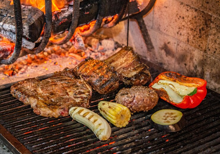 Foto varios tipos de carne, pimienta, berenjenas de maíz y plátanos asados en una parrilla