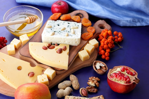 Varios tipos de composición de queso con panecillos de miel y una servilleta azul sobre un fondo azul Dos tipos de queso con frutas, bayas, nueces y frutos secos sobre una tabla de madera