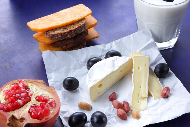 Varios tipos de composición de queso en un primer plano de fondo azul Quesos con frutas nueces y un vaso de leche sobre papel pergamino