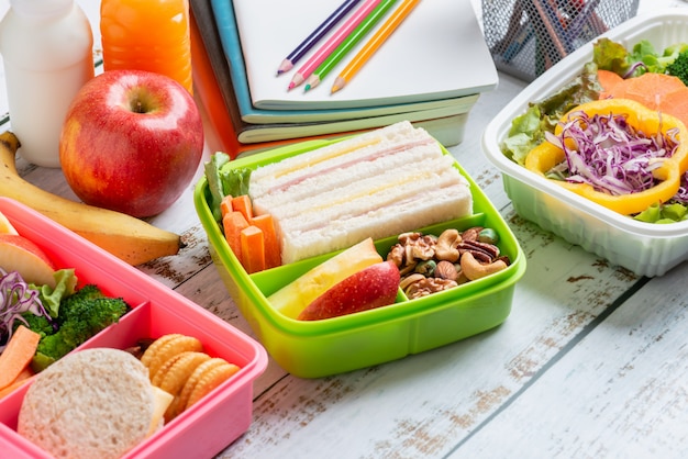 Foto vários tipos de lancheiras saudáveis de sanduíche. garoto bento pack para escola conjunto em pacote plástico, caixa de salada, banana e maçã com suco de laranja, leite.