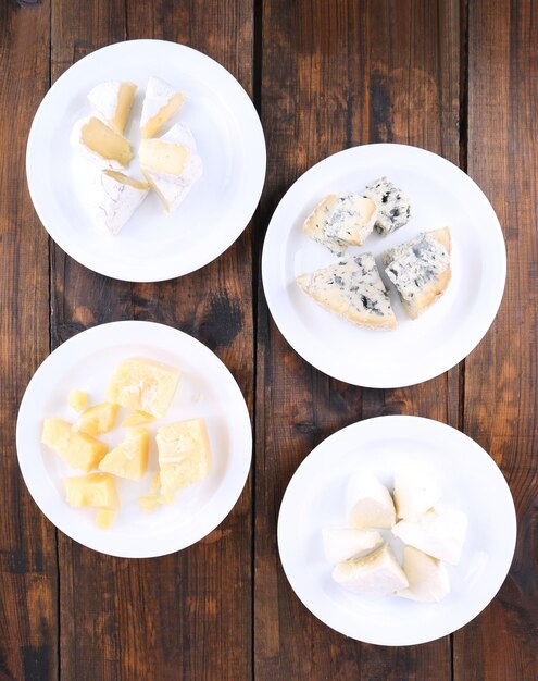 Foto vários tipos de queijo em pratos sobre fundo de mesa de madeira